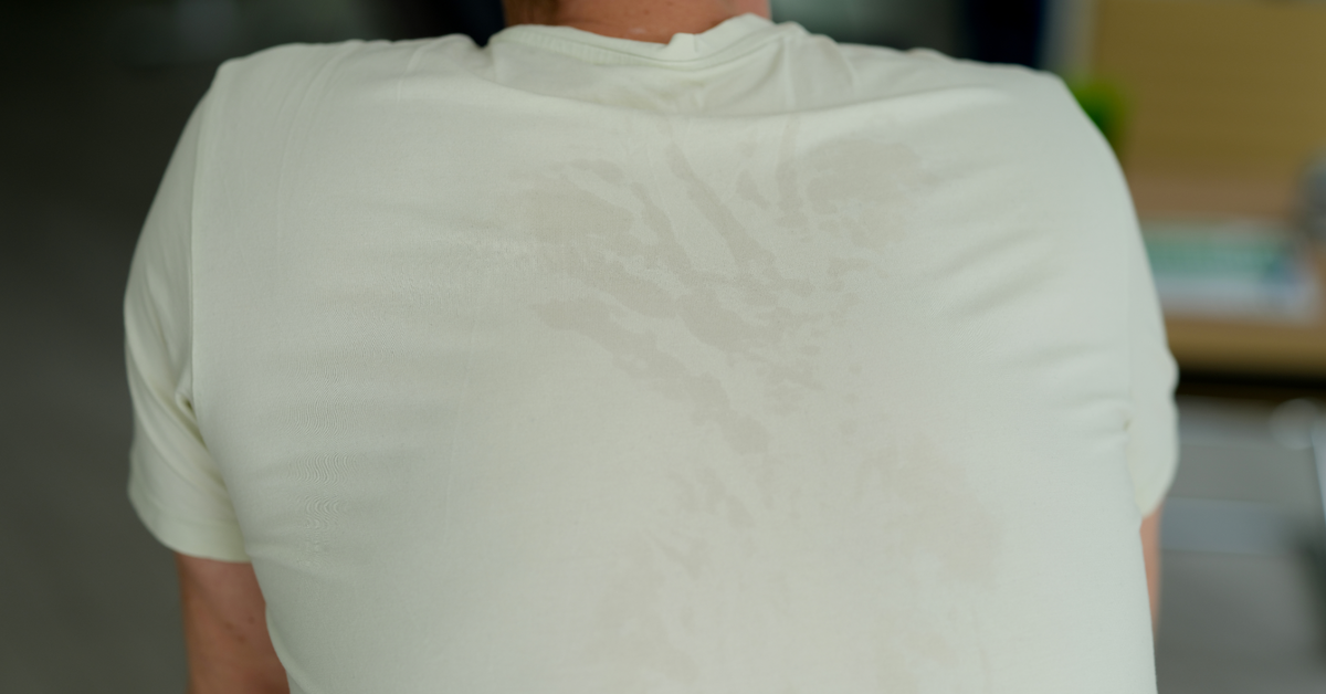 The back of a man's white t-shirt showing a large visible sweat patch between his shoulders, a common sign of excessive sweating