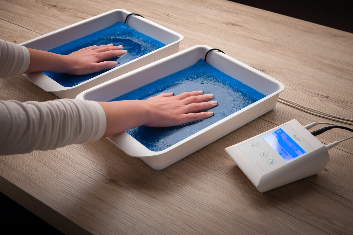 Hands resting in two Saalio® tap water trays beside the iontophoresis control unit