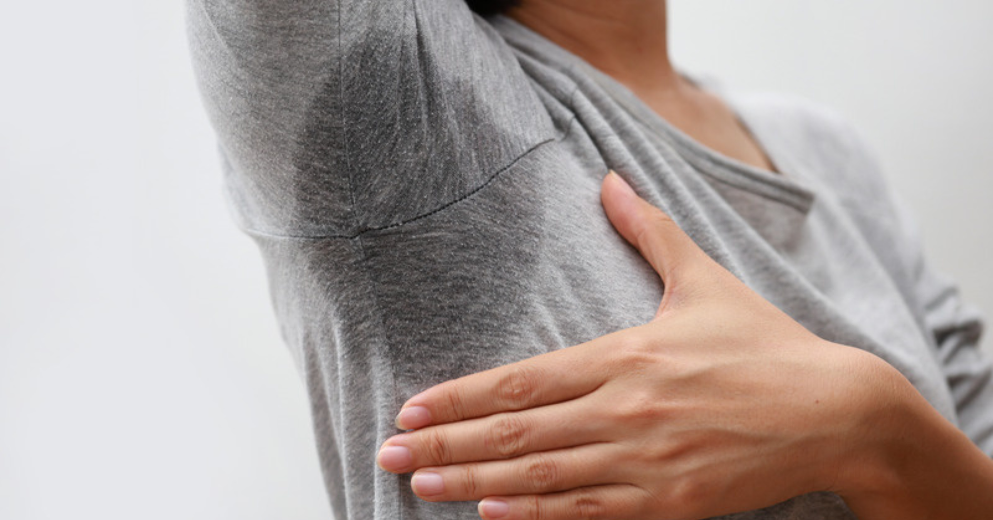Person showing an underarm sweat mark on a grey shirt, illustrating axillary hyperhidrosis