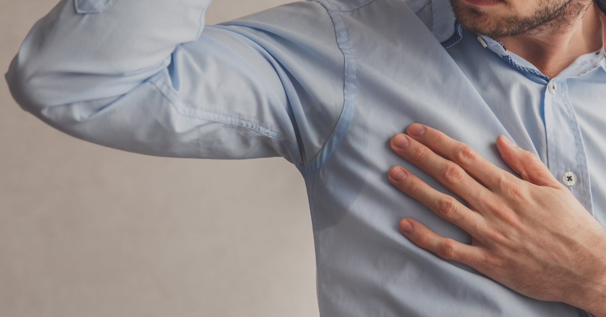 A man in a light blue shirt lifting his arm to check an underarm sweat mark, illustrating common questions about iontophoresis