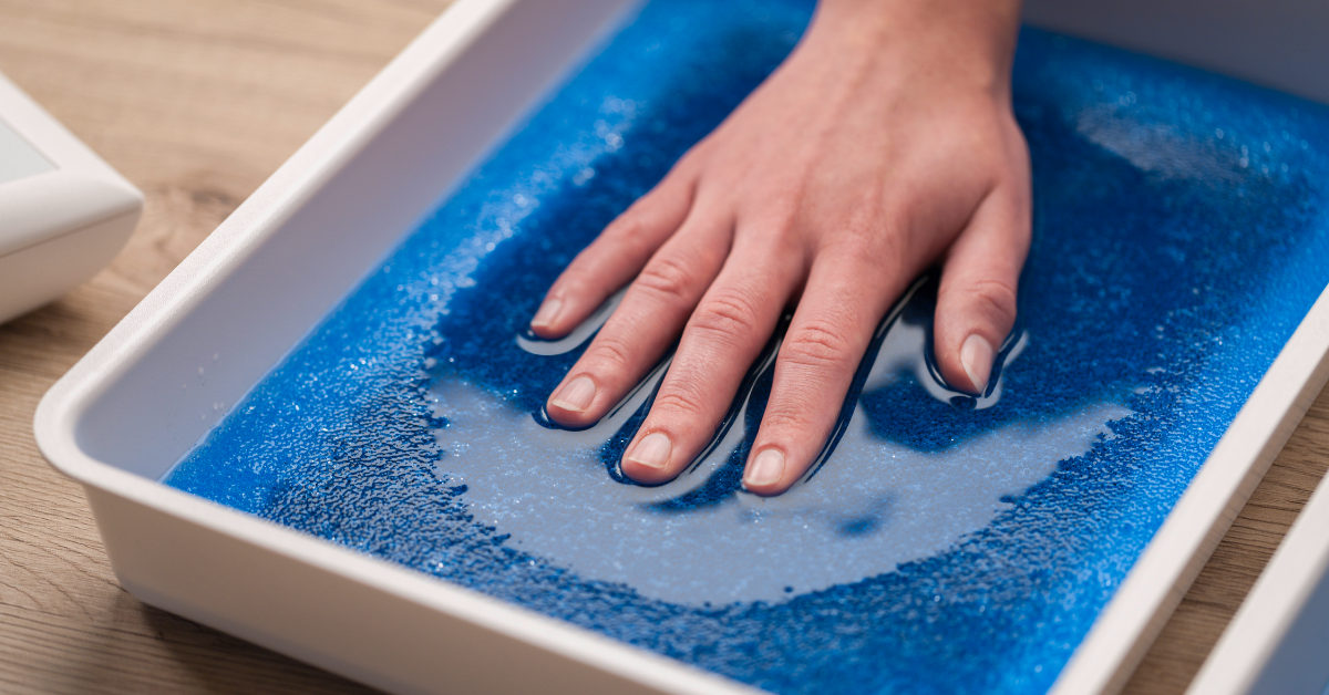 A hand submerged in a shallow tray of water during an iontophoresis treatment session for sweaty hands, with a silicone electrode mat visible beneath the water.