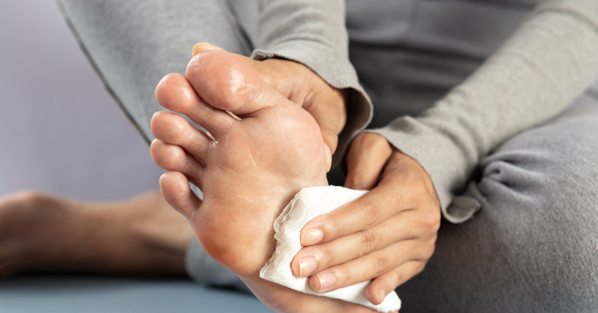 A person wiping the sole of their visibly sweaty foot with a tissue, illustrating the daily impact of plantar hyperhidrosis (sweaty feet)