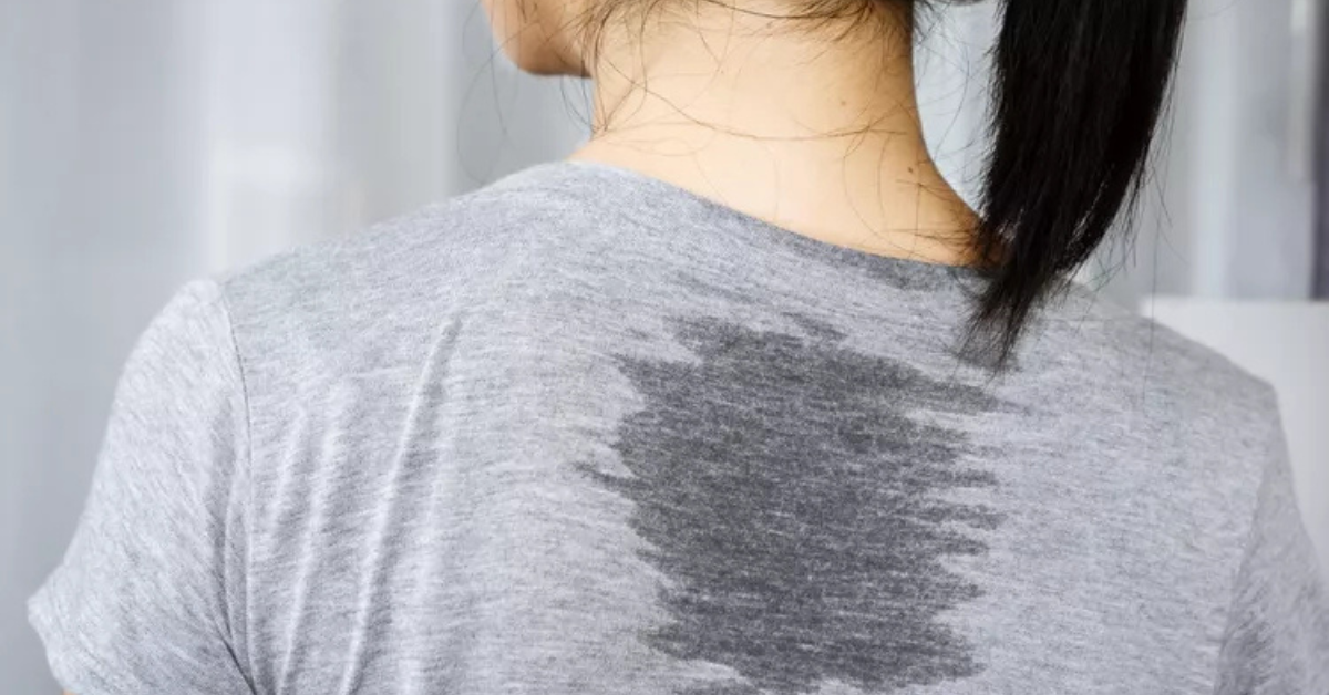 The back of a woman's grey t-shirt showing a large visible sweat patch between her shoulders, a common sign of excessive sweating.
